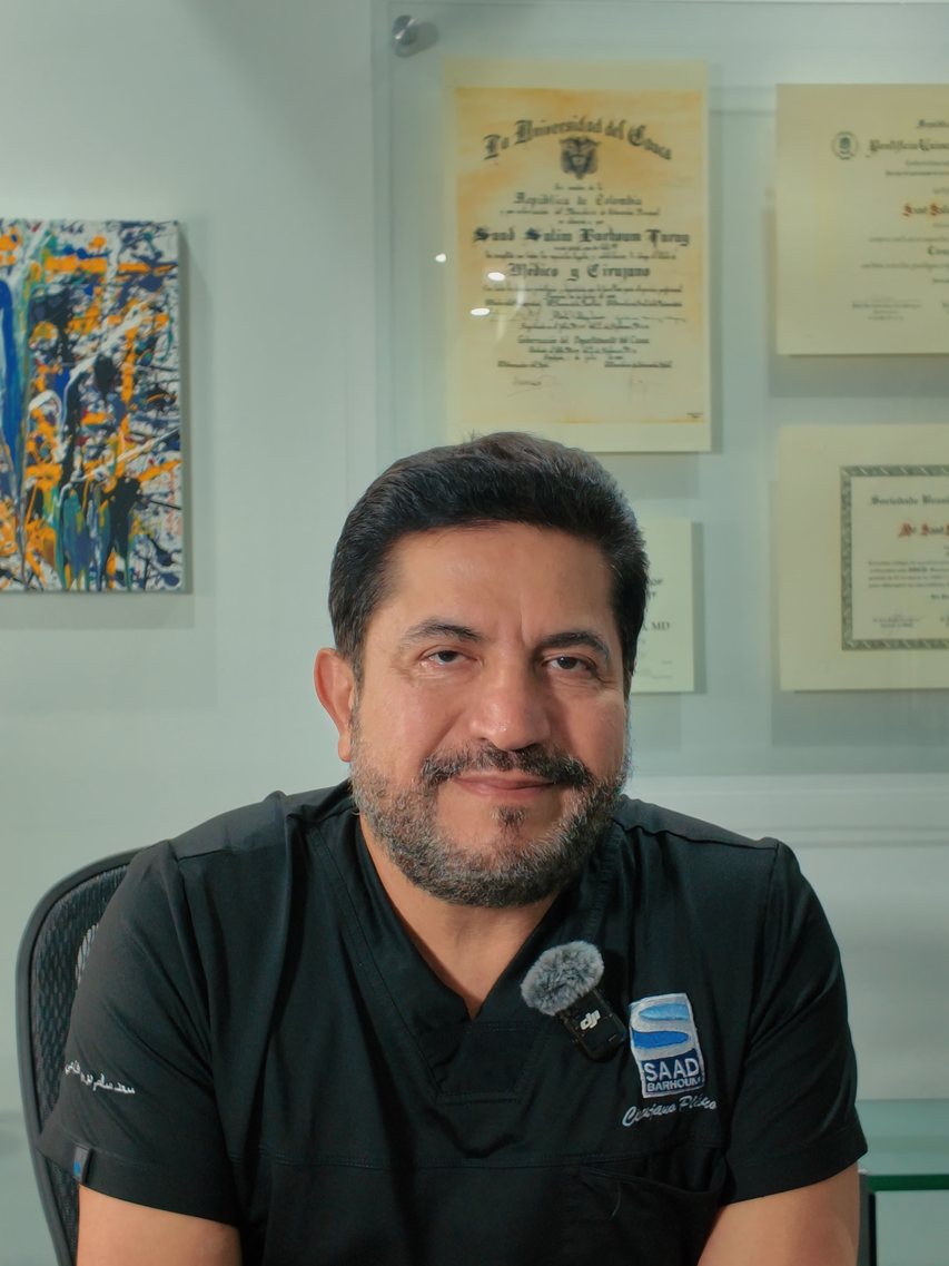 El Dr. Saad Barhoum sentado en el escritorio de su consultorio en Cali, con uniforme negro.
