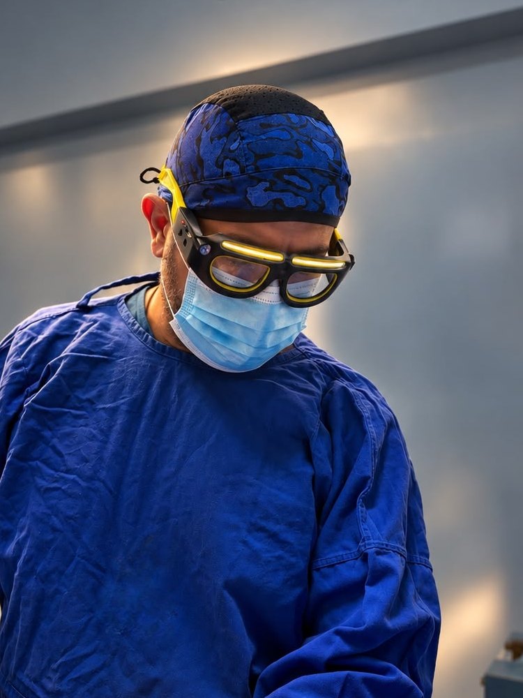 El Dr. Saad Barhoum en el quirófano, con lupas quirúrgicas y gorro azul. No se ve a ninguna paciente.